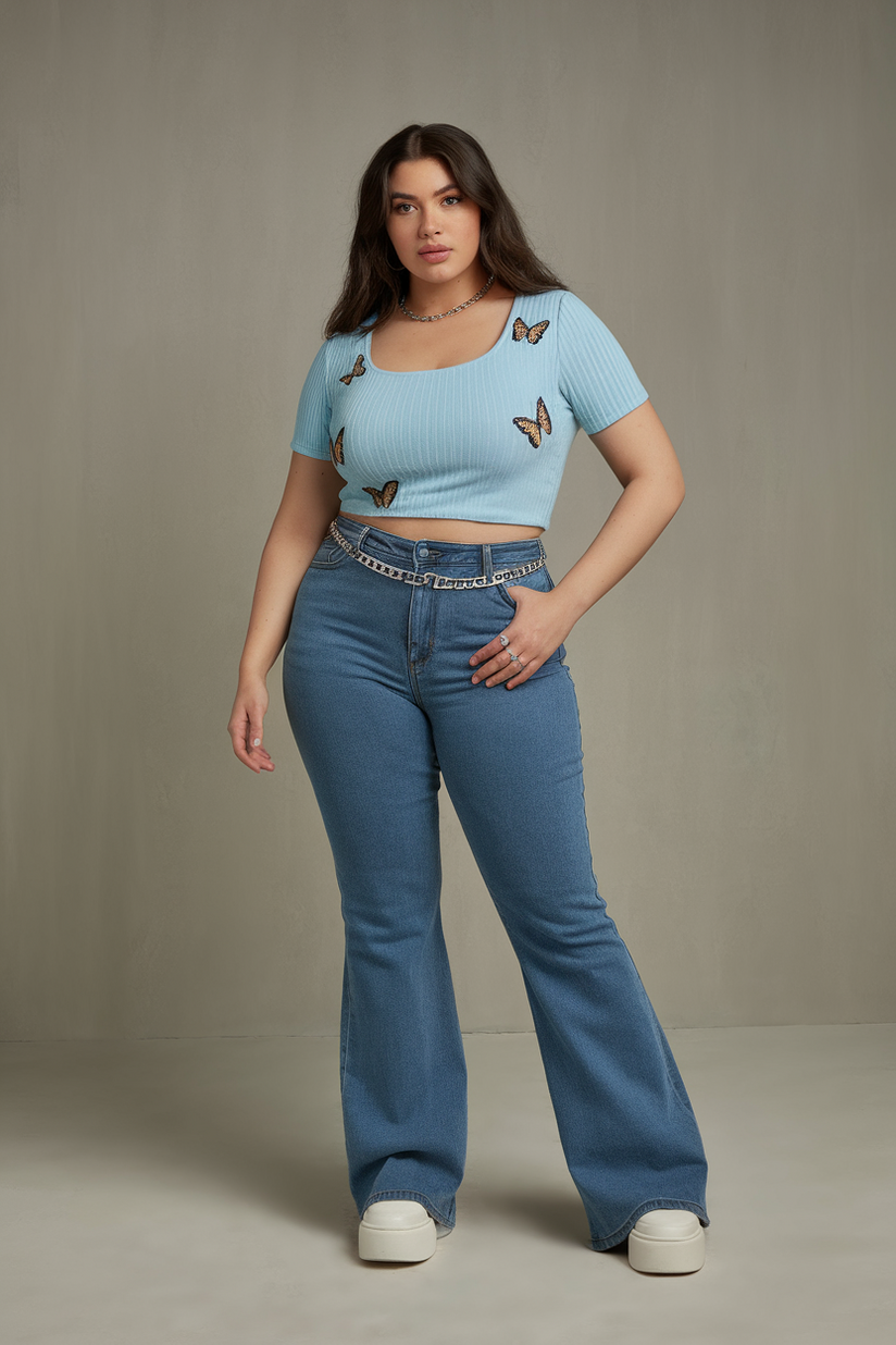 Plus-size woman in a blue ribbed crop top with flared jeans and platform sneakers, standing against a gray background.