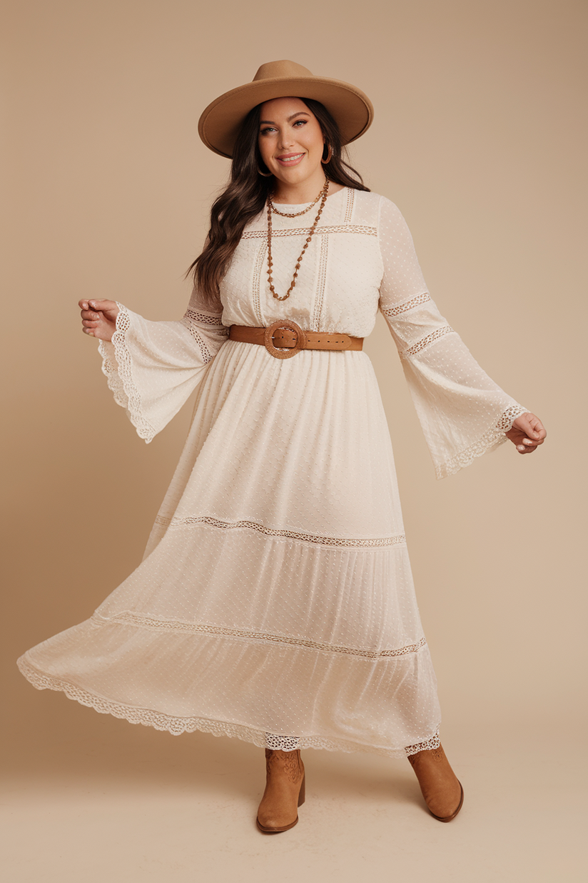 Plus-size woman in a white maxi dress with lace details and tan ankle boots, standing against a beige background.