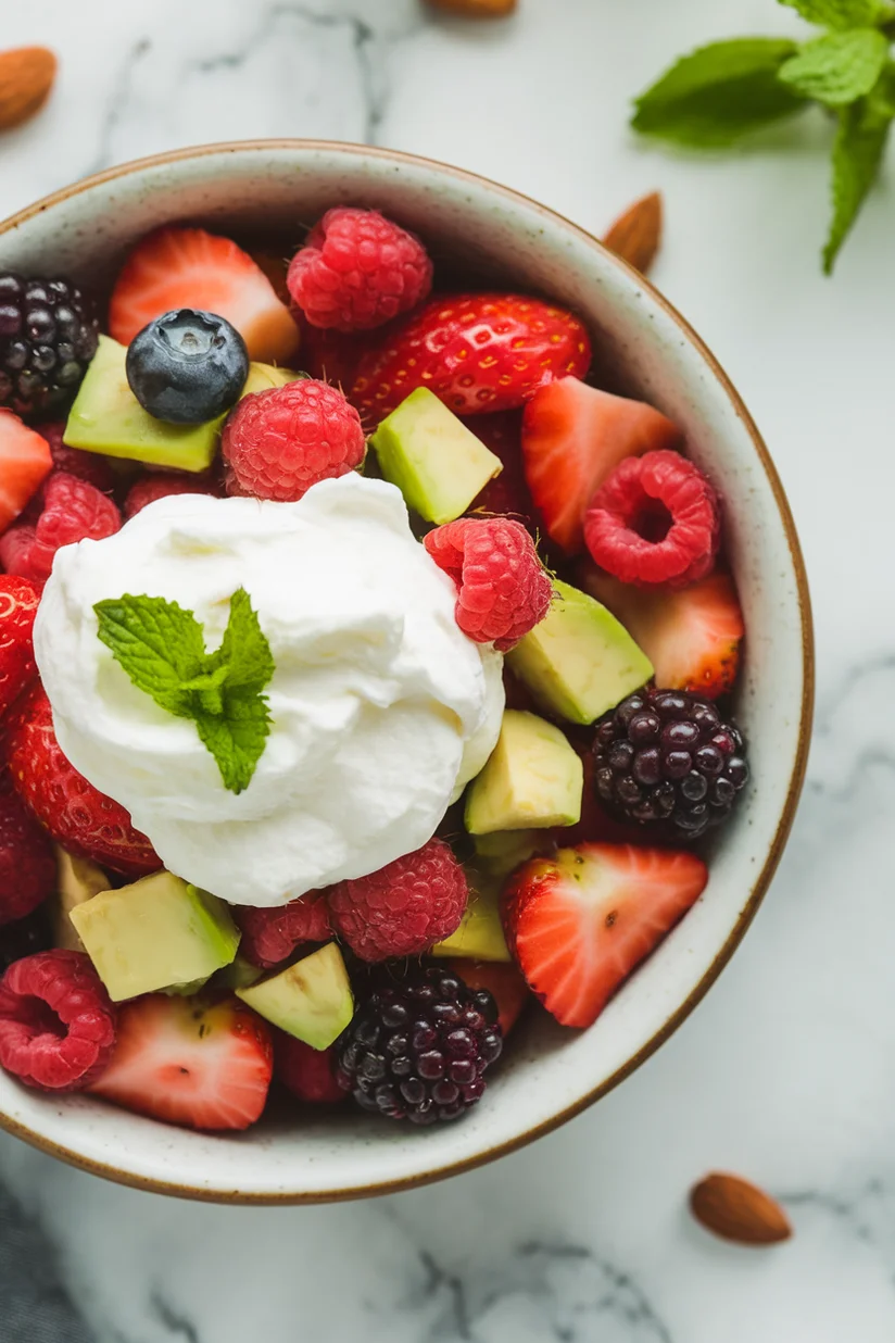 Keto fruit salad with berries and avocado on white marble countertop.